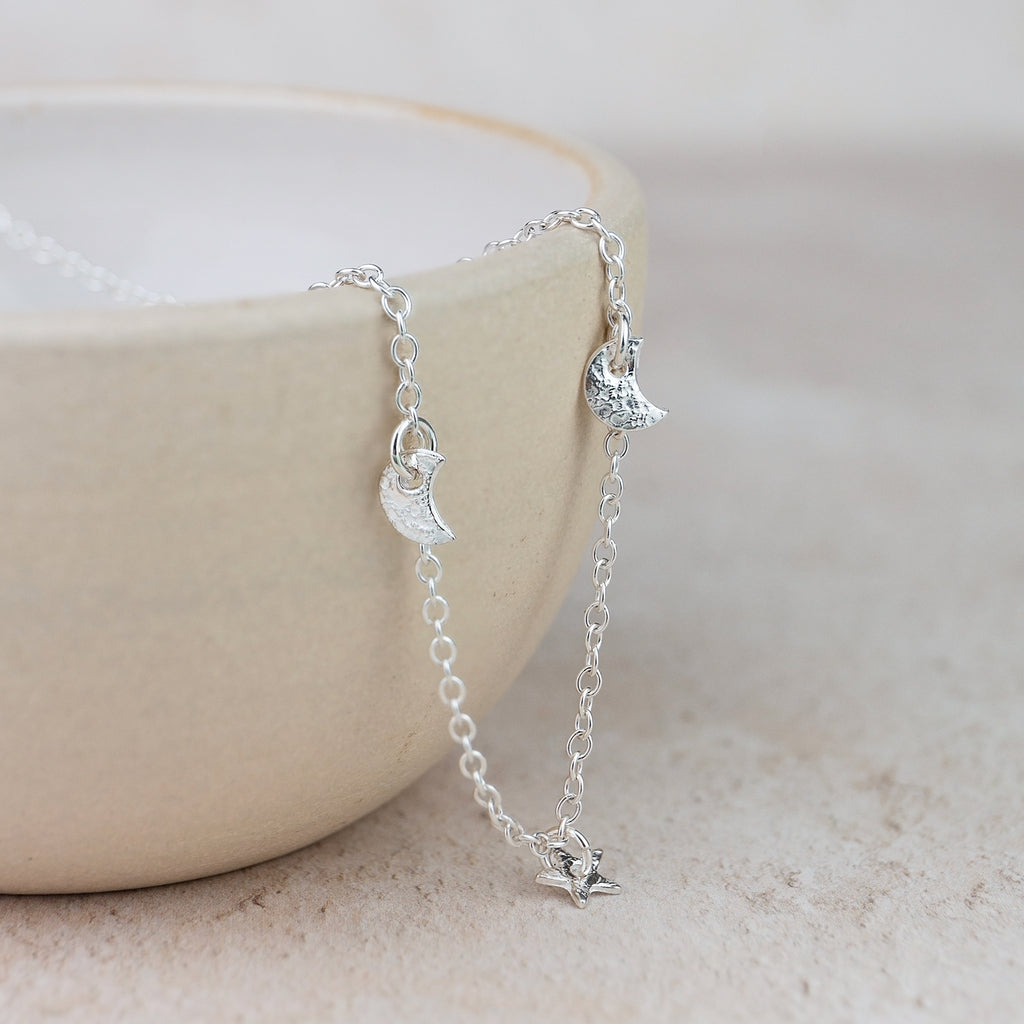 Silver necklace with moon and star charms on a light background