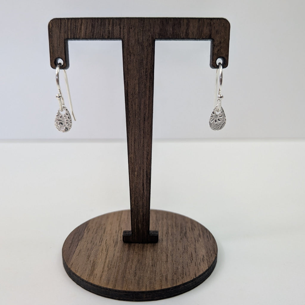 Wooden earring stand with two silver earrings on a white background